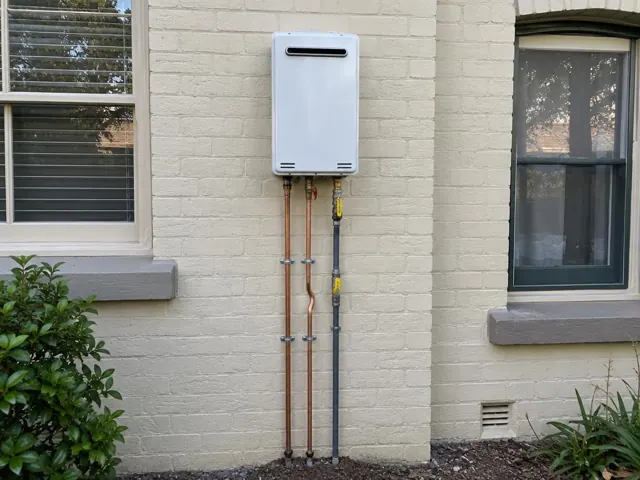 Wall-mounted hot water unit with copper pipework on a painted brick exterior wall in Roseville