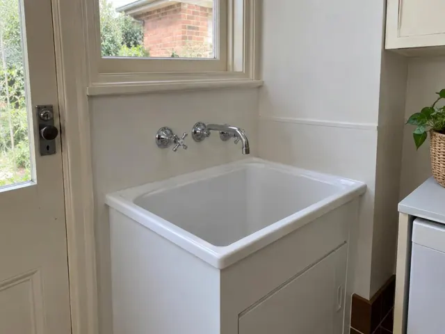 White laundry sink with new wall-mounted tap beside a door and window in Lindfield